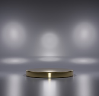 A metallic platform is centered in a minimalistic setting with a reflective surface. Soft, diffused lighting creates circular patterns on the background wall, enhancing the focus on the central stage. The ambiance is sleek and modern, with a hint of elegance.