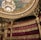 An opulent theater interior featuring grand architectural details with intricate gold ornamentation. A massive chandelier hangs from the ornate ceiling, which displays colorful artwork. The seating area is plush, with rows of luxurious red seats.